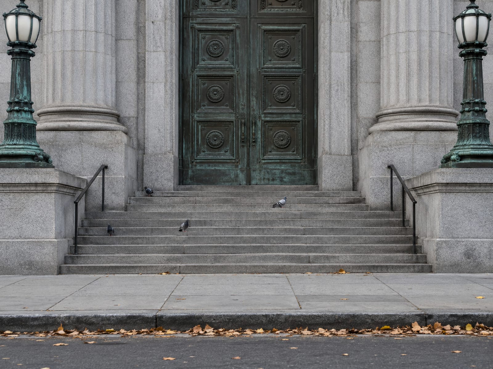 The empty granite steps and shut bronze doors of a civic building on a quiet Saturday morning, a few pigeons and fallen leaves